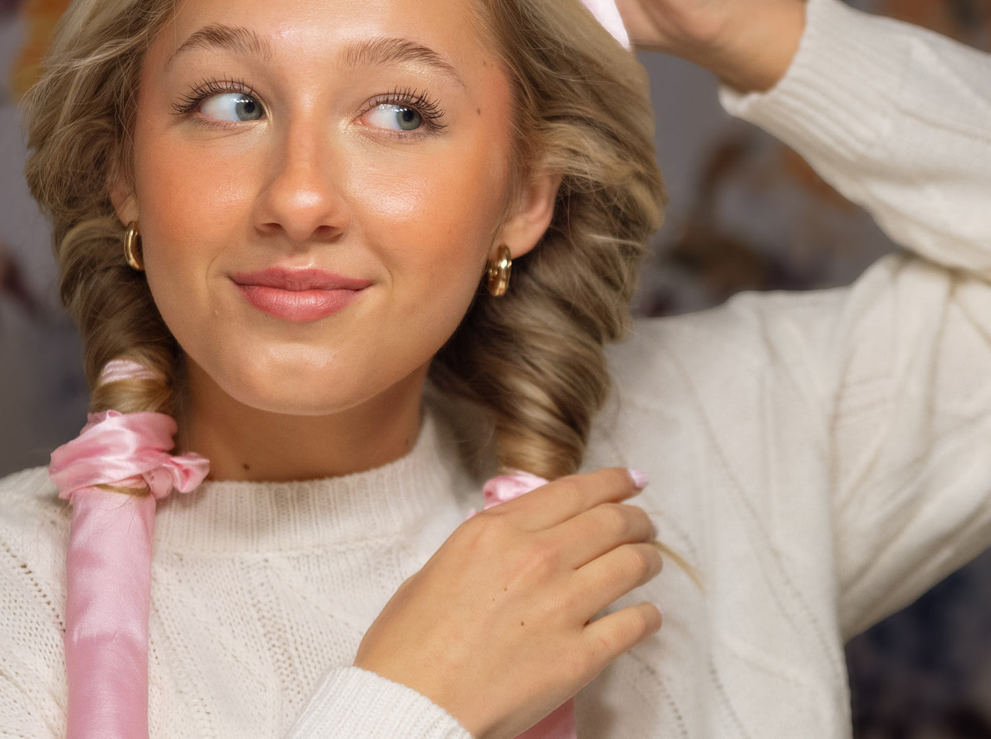 Close-up of woman wearing pink satin heatless curlers, gently twisting her hair for overnight, no-heat curls that prevent heat damage.
